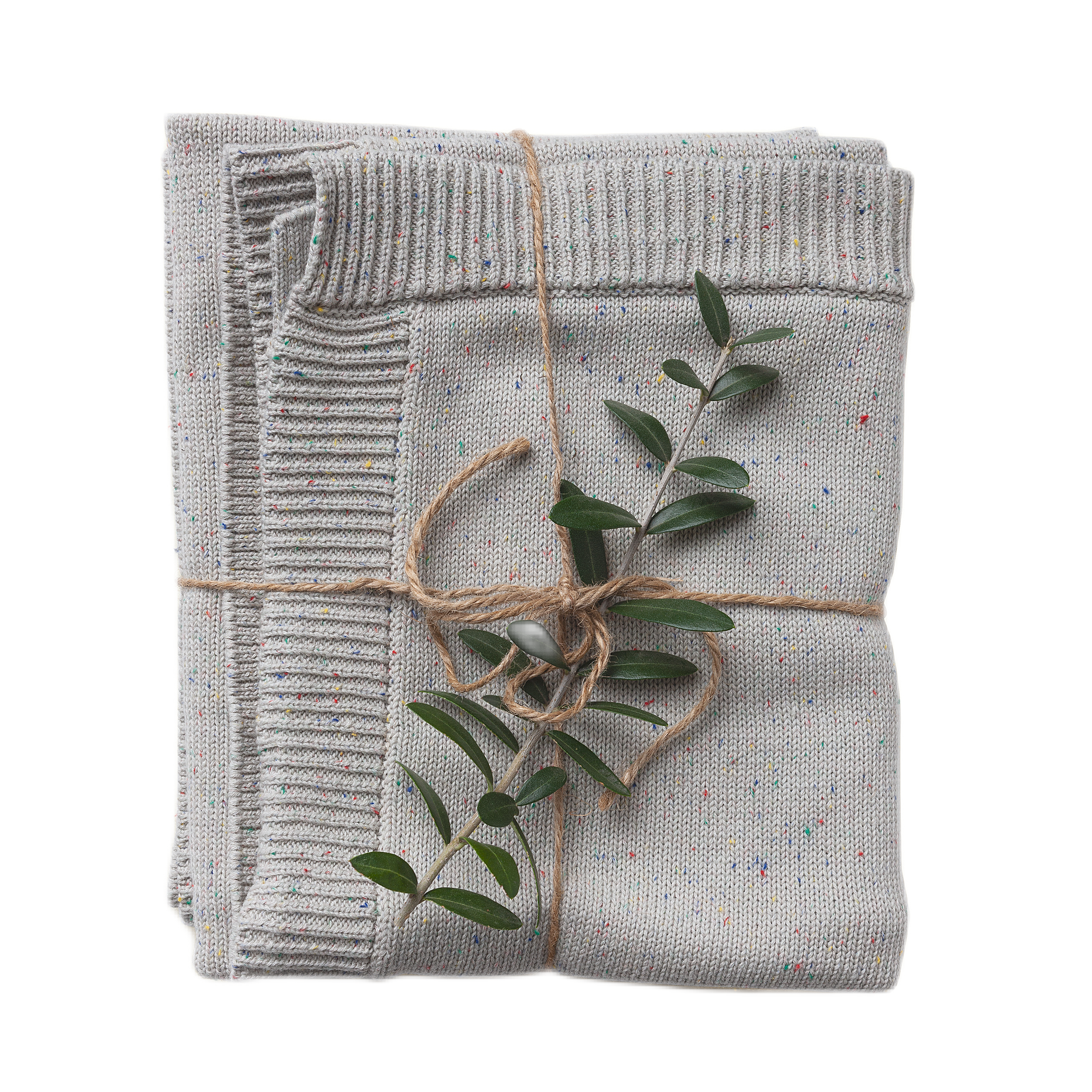 A folded confetti-speckled knit blanket in shades of gray, tied with a string, featuring a small branch of green leaves protruding from the fold.