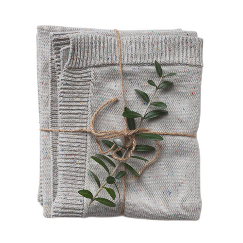 A folded confetti-speckled knit blanket in shades of gray, tied with a string, featuring a small branch of green leaves protruding from the fold.